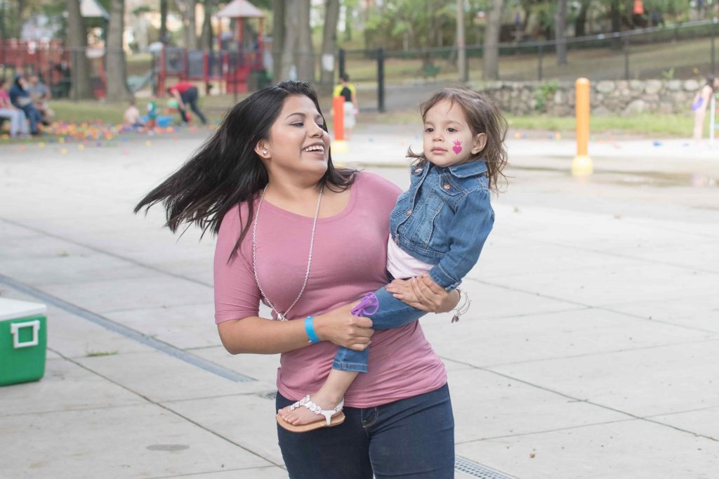 Woman in pink shirt carrying small child in a denim jacket on her right hip