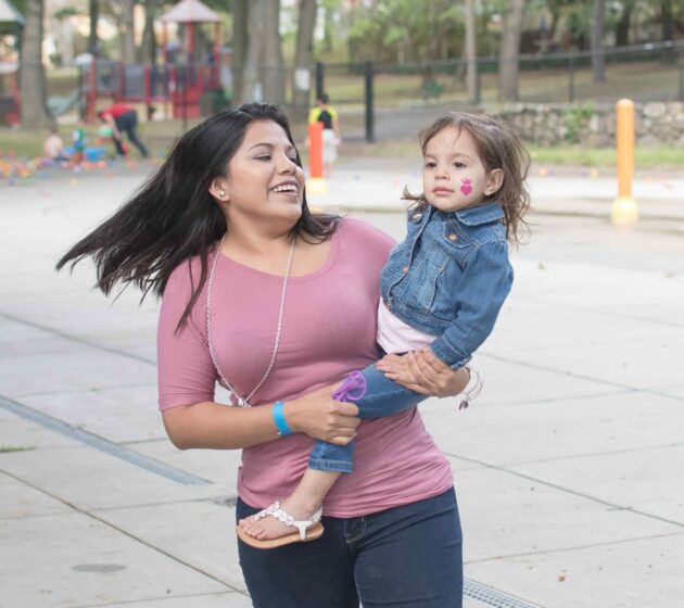 Woman in pink shirt carrying small child in a denim jacket on her right hip
