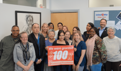 sixteen people smilling holding a sign that says they were granted one hundred thousand dollars