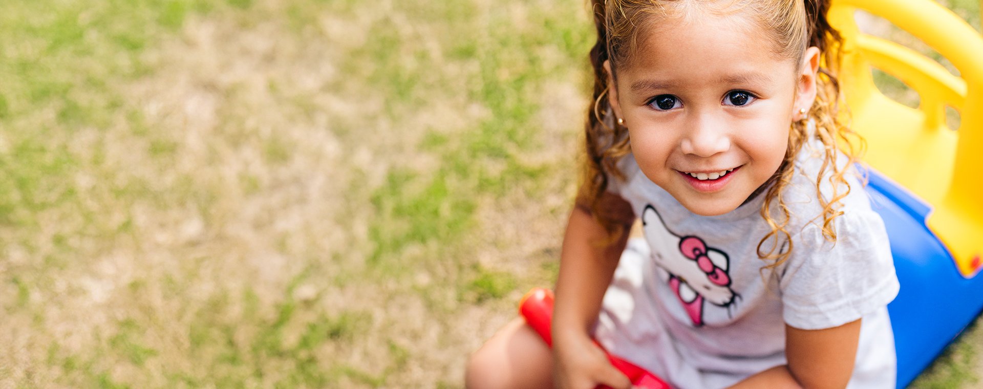 A smiling young girl with curly hair plays on a colorful slide