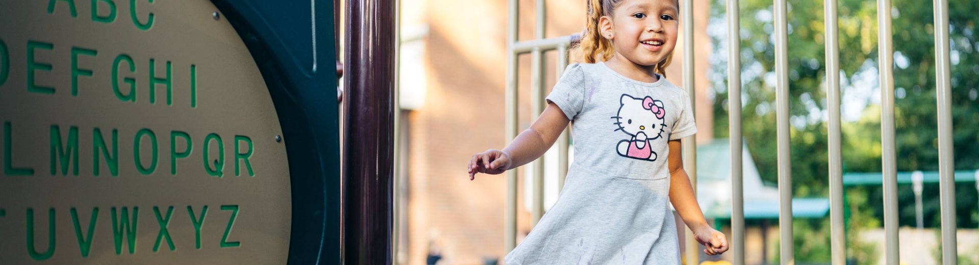 A smiling young girl runs across a playground beside an alphabet panel