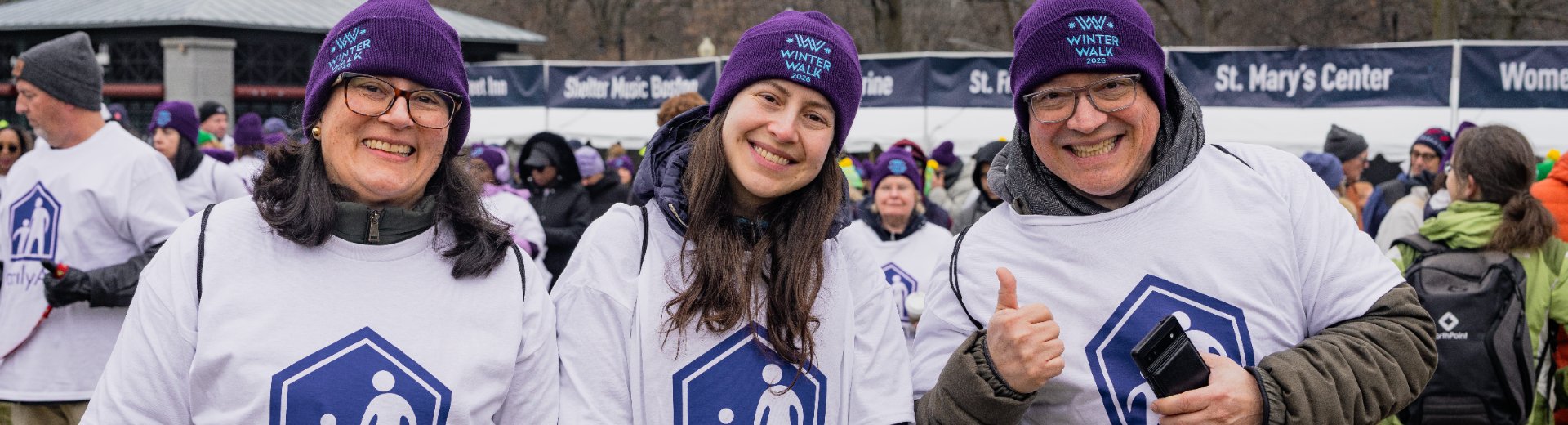 Three smiling FamilyAid team members in Winter Walk beanies at the event on Boston Common