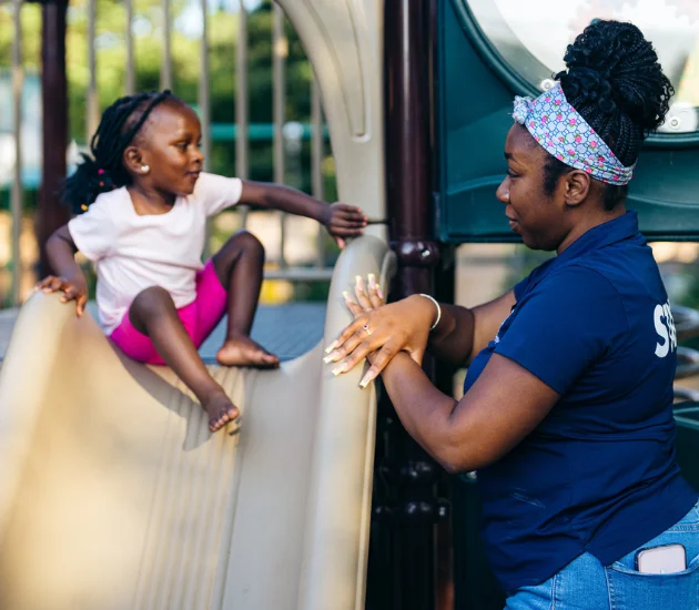 a young girl talks with a FamilyAid staff member on a playground